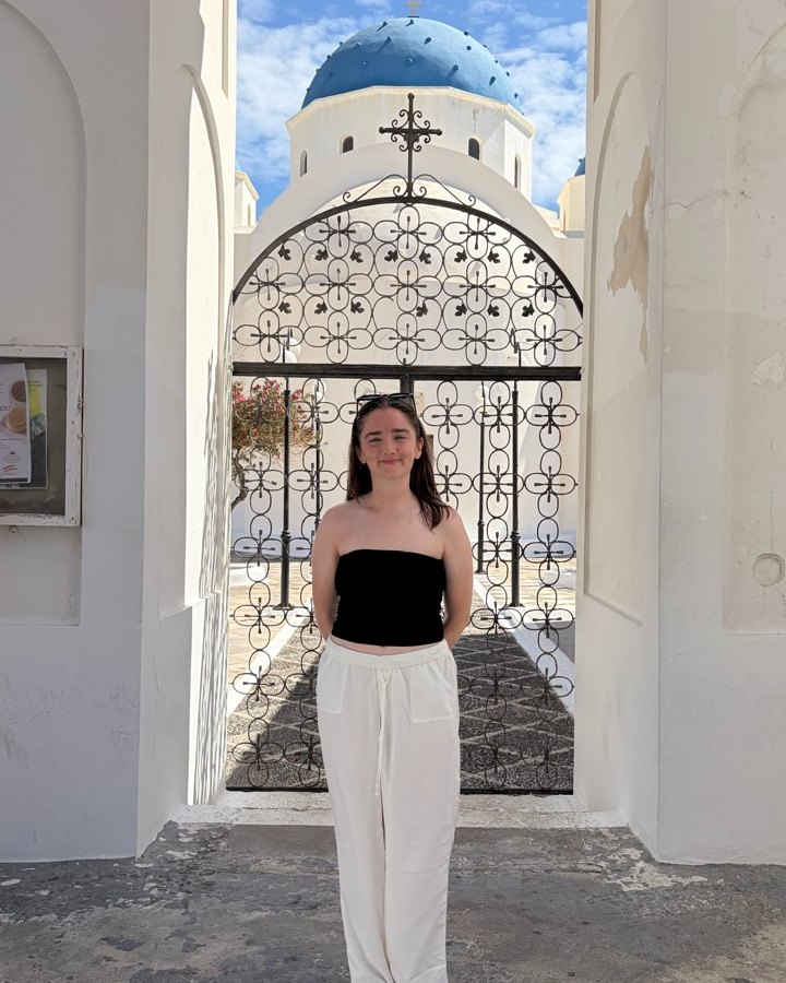 Saoirse standing in front of a whitewashed church with a blue dome in Greece